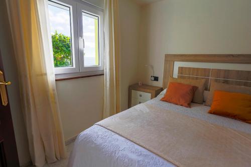 a bedroom with a bed with orange pillows and a window at Apartamento Playa de Lires in Cee