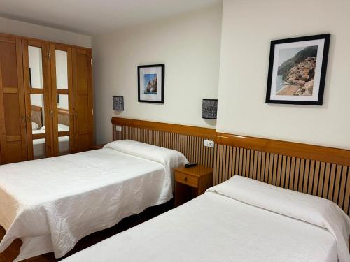 two beds in a hotel room with white sheets at Pensión Mencia in Lugones
