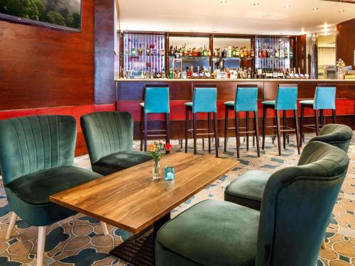 a bar with blue chairs and a wooden table at Mercure Chester Abbots Well Hotel in Chester