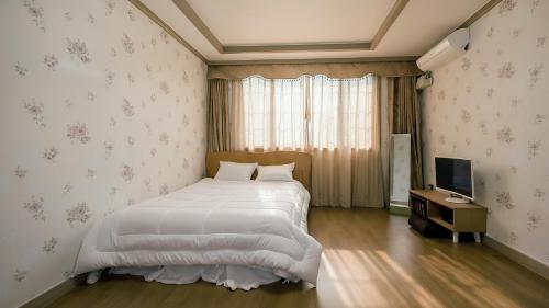 a bedroom with a white bed and a television at Samcheok Eoulim Pension in Samcheok