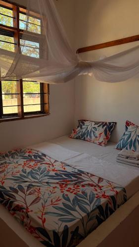 a bedroom with a large bed with a comforter and two windows at Shalom Homestay in Kilindoni