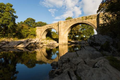 a stone bridge over a river with its reflection in the water at Woodclose Park in Kirkby Lonsdale