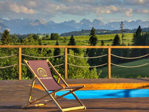 a chair sitting on a deck with a view of the mountains at Osada Wichrówka domki ze strefą SPA, basenem letnim i widokiem na góry in Dursztyn