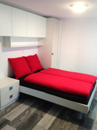 uma cama vermelha num pequeno quarto com armários brancos em Haus Rosa em Zermatt