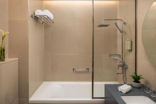 a bathroom with a shower with a tub and a sink at Bloom Arjaan by Rotana in Abu Dhabi