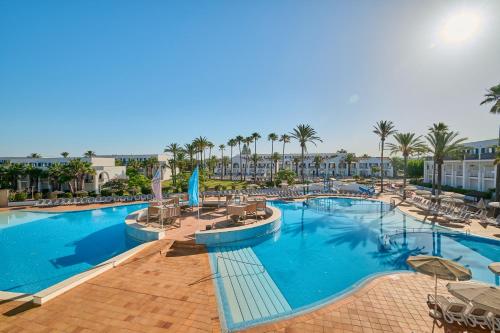 a pool at a resort with chairs and palm trees at Grupotel Mar de Menorca in Es Canutells
