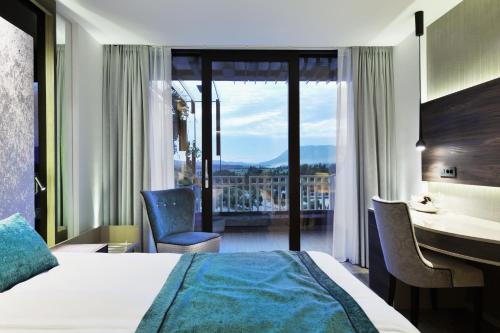 a hotel room with a bed and a desk with a view at Postojna Cave Hotel Jama in Postojna