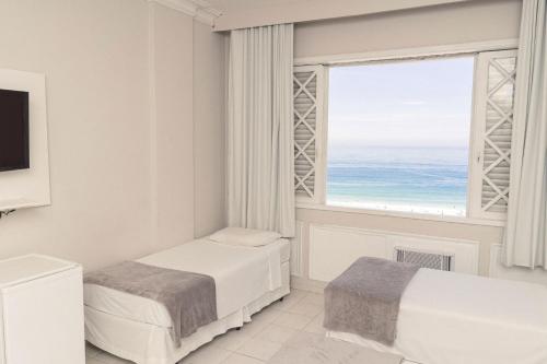 a bedroom with two beds and a window with the ocean at CLH Suites Domingos Ferreira in Rio de Janeiro