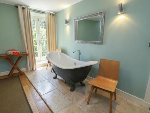 a bathroom with a tub and a chair and a mirror at Clynnog House in Dwyran