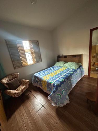 a bedroom with a bed and a chair and a window at Casa da Conceição in Capitólio