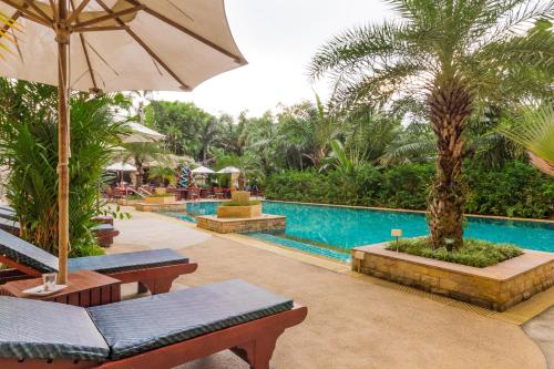 a resort pool with benches and an umbrella at Dasiri Beach Apartment Premium in North Pattaya