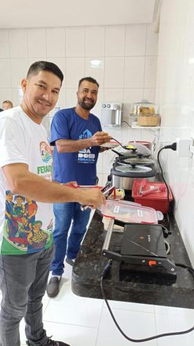 two men standing in a kitchen preparing food on a stove at Pousada Panorama Palace in Santa Maria da Vitória