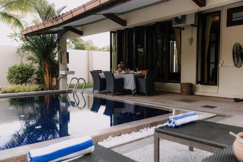 a person sitting at a table next to a swimming pool at The Villa - Private Pool near Tanjung Rhu Beach by WOW Holiday Homes in Kuah