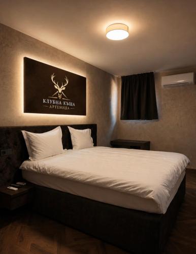 a bedroom with a large bed with a sign on the wall at Клубна къща Артемида - Стая in Pravets