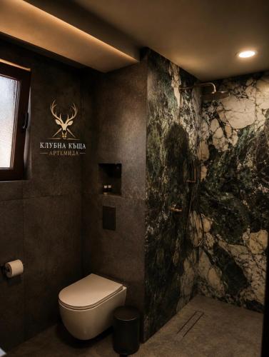 a bathroom with a toilet and a stone wall at Клубна къща Артемида - Стая in Pravets