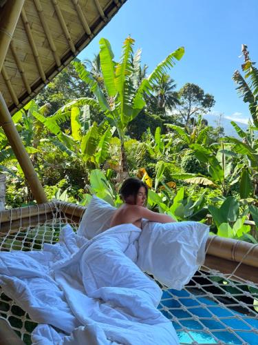 a man laying in bed under a blanket at Bamboo Garden Villa Sidemen - Private Pool & Nature View in Selat