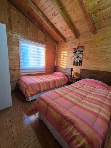 a bedroom with two beds in a log cabin at Cabañas Alfa Colbun Machicura in Linares