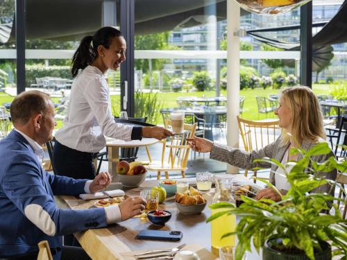 a woman serving people at a table in a restaurant at Novotel Lausanne Bussigny in Lausanne
