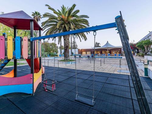 a playground with a swing set and a tree at Novotel Setubal in Setúbal