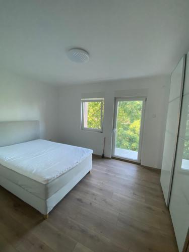 a white bedroom with a bed and a wooden floor at Kuća za odmor Aranđelovac in Arandelovac
