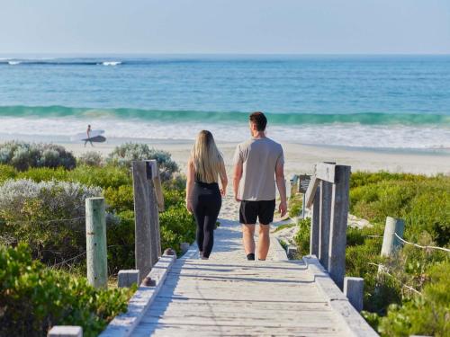 a man and woman walking down a boardwalk to the beach at Pullman Bunker Bay Resort Margaret River in Dunsborough