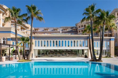 a swimming pool in front of a building with palm trees at Meliá Isla Canela in Isla Canela