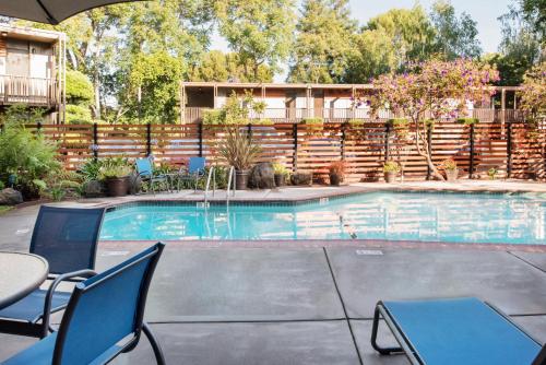a swimming pool with chairs and a table and a fence at The Creekside Inn in Palo Alto