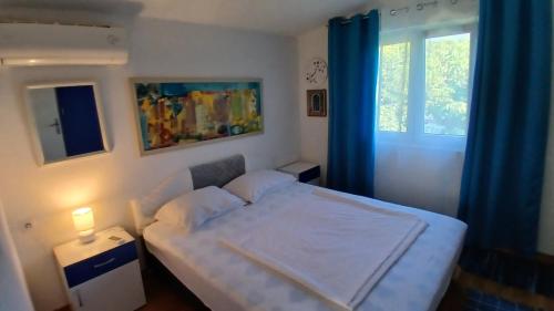 a bedroom with a bed with blue curtains and a window at Apart SRDJ&MAR in Dobra Voda