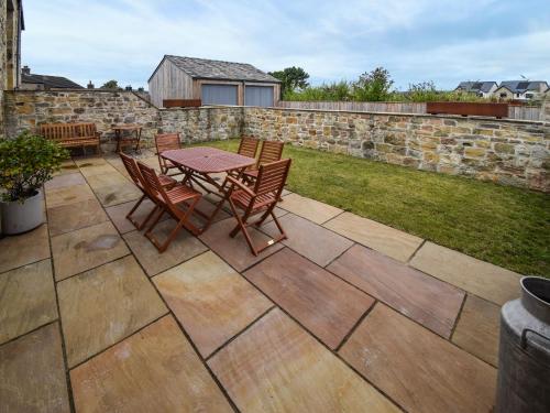 a patio with a table and chairs and a stone wall at Hay Barn in Carnforth