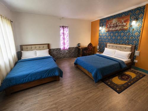 two beds in a room with blue sheets and a window at Lungta Homes in Bomdila