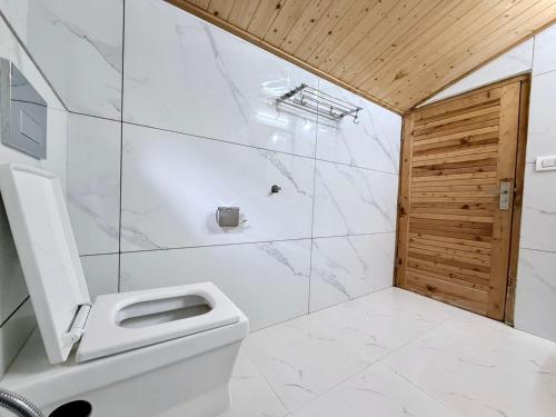 a bathroom with a white toilet and a wooden door at Hotel Mount Manali - The Cozy Stay in Vashisht