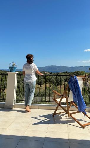 a woman standing on a balcony with a chair at Horizon House, with Olive Grove and a small Vineyard in Amarynthos