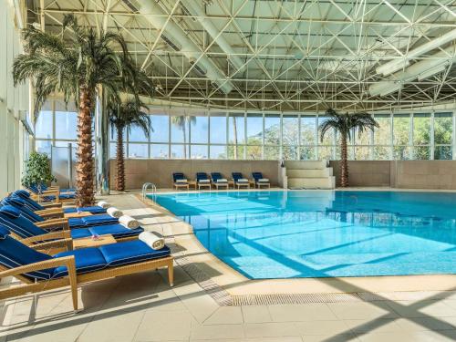 a large swimming pool with blue chairs and palm trees at Mövenpick Hotel Al Khobar in Al Khobar
