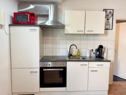 a kitchen with white cabinets and a red microwave at Mini Apartment mit Garten und Küche in Ilbenstadt