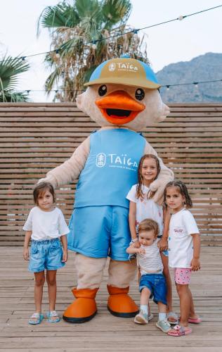 a group of children standing next to a large duck mascot at TAIGA Bassegoda Park in Albanya