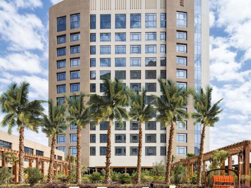 a tall building with palm trees in front of it at Movenpick Hotel and Residences Riyadh in Riyadh