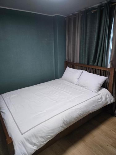 a bed with white sheets and a green wall at Art and Stay in Suncheon