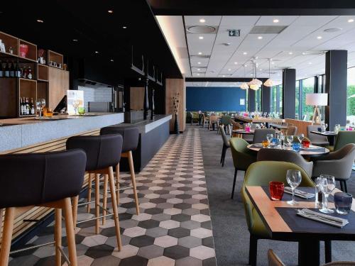 a restaurant with a bar and tables and chairs at Novotel Caen Côte de Nacre in Caen