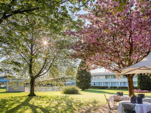 a park with tables and trees and a building at Novotel Lille Aéroport in Lesquin