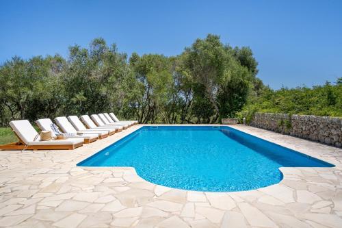 a swimming pool with lounge chairs next to a stone wall at Finca Biniatzau by 3VILLAS in Alaior