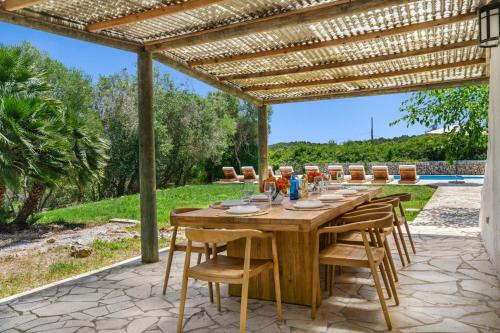 a wooden table and chairs under a wooden pergola at Finca Biniatzau by 3VILLAS in Alaior