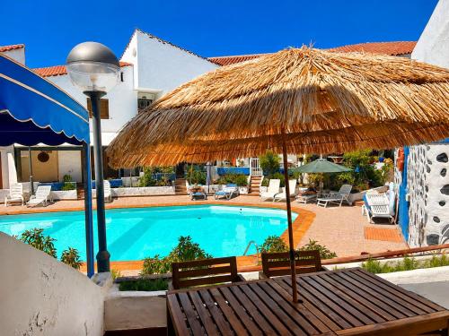 a pool with a straw umbrella and a table and chairs at El Molino Agaete in Puerto de las Nieves