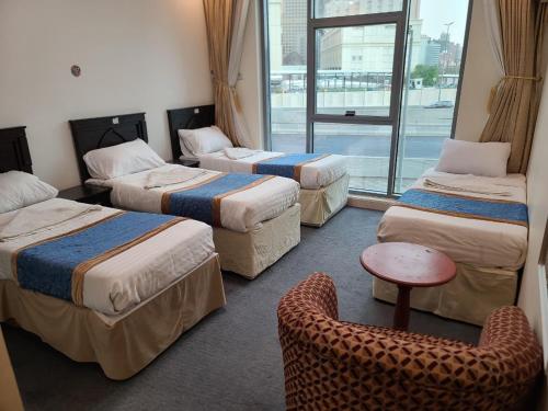 a room with three beds and a chair and a window at Qimmat AlAwali Hotel in Az Zahrāʼ