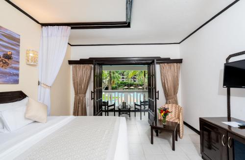a bedroom with a bed and a tv and a balcony at PrideInn Flamingo Beach Resort & Spa Mombasa in Mombasa