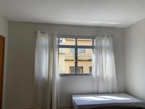 a window with white curtains and a bed in a room at Apartamento central in Domingos Martins
