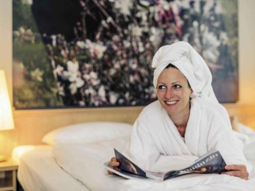 Eine Frau liegt im Bett und liest ein Buch in der Unterkunft Mercure Hotel Erfurt Altstadt in Erfurt