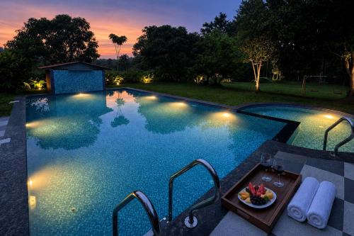 a swimming pool at night with a plate of food on a table at Firefly By The River with Breakfast - Coorg in Kushālnagar