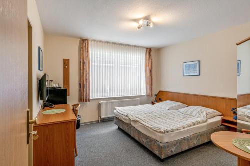a bedroom with a bed and a desk and a television at Hotel Zum Wikinger in Dornum