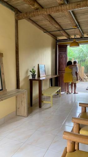 two people standing in a room with a table and a bench at Casa da Raposa in Iguaíba