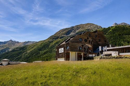 a building in a field with mountains in the background at Blu Senales Active & Family Resort in Maso Corto